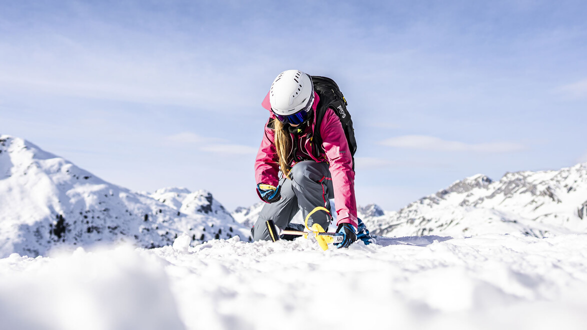 Person in roter Jacke bei Lawinensuchübung im verschneiten Gelände / Person in red jacket during avalanche search in snowy terrain