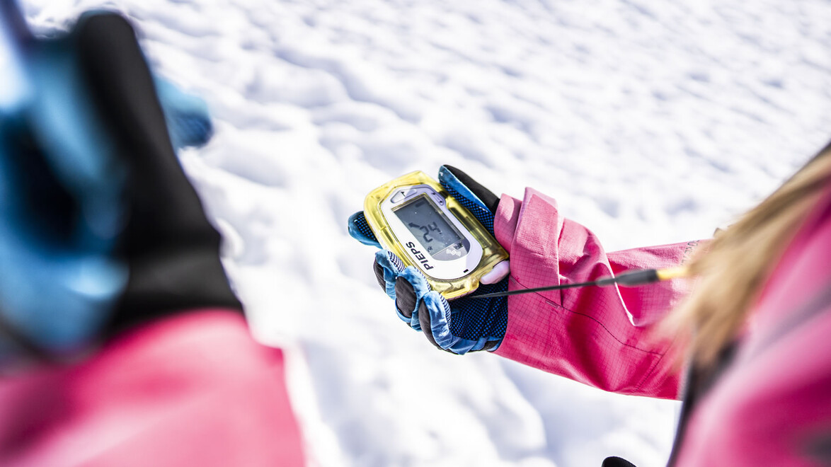 Nahaufnahme eines LVS-Geräts in der Hand einer Person im Schnee / Close-up of avalanche transceiver in person's hand in snow