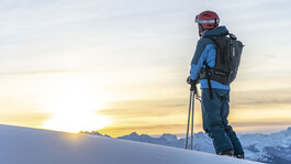 Ski tourer gazes at the snowy Alps during sunrise.