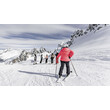 Eine Skifahrerin nähert sich einer Gruppe am Pistenrand, umgeben von verschneiten Gipfeln / A skier approaches a group at the edge of the slope, surrounded by snowy peaks