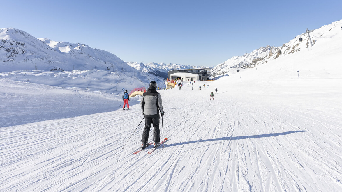 Person fährt alleine auf einer breiten, frisch präparierten Piste mit Blick auf das Tal / A person skis alone on a wide, freshly groomed slope with a view into the valley
