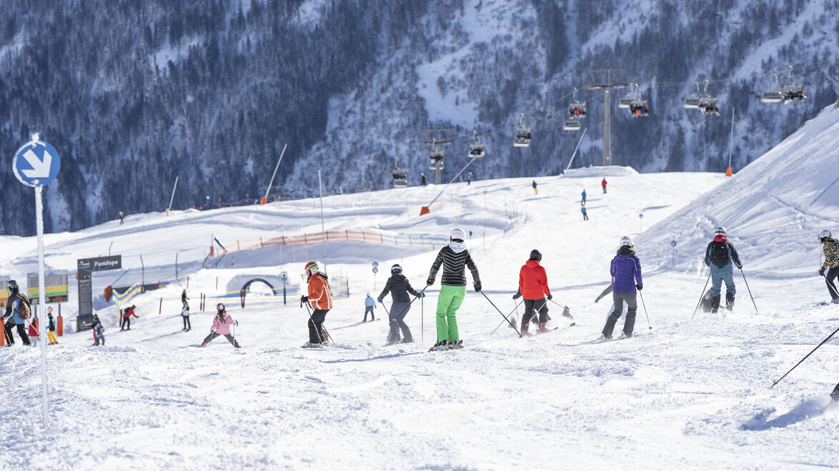 Zahlreiche Skifahrer:innen auf einem breiten Übungshang bei einer Skischule / Numerous skiers on a wide practice slope at a ski school