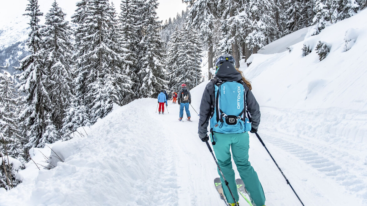 Personen wandern mit Tourenski auf einem verschneiten Weg durch einen Winterwald / People are ski touring on a snow-covered trail through a winter forest
