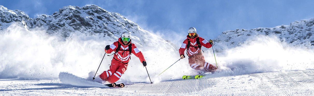 Two skiers in red carving on freshly groomed slopes in St. Anton am Arlberg.