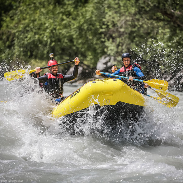 Two men laugh while rafting through wild water, surrounded by splashing spray and thrill.