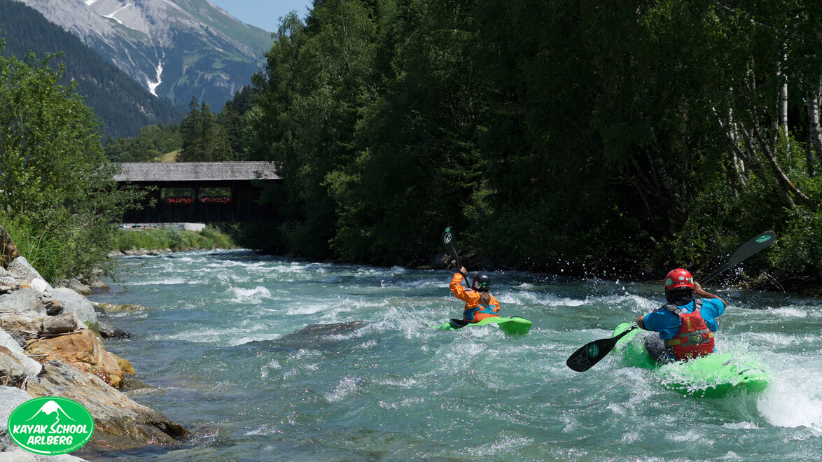 Kajakfahrer auf einem Fluss mit Blick auf eine überdachte Holzbrücke im Hintergrund / Kayakers on a river with a covered wooden bridge in the background