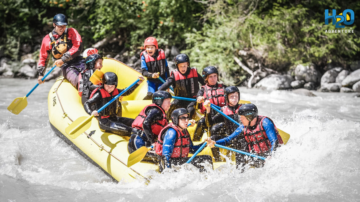 Eine Gruppe Menschen beim Wildwasser-Rafting in einem gelben Schlauchboot auf einem spritzenden Fluss / A group of people whitewater rafting in a yellow inflatable boat on a splashing river