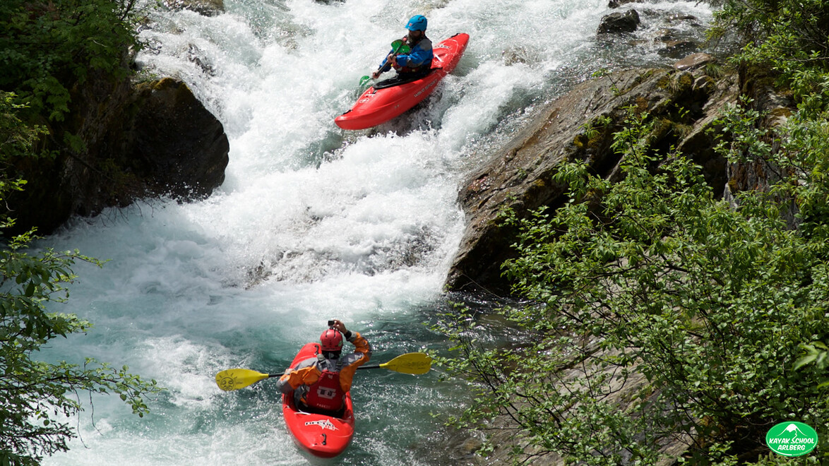 Zwei Kajakfahrer fahren eine enge Stromschnelle mit steilen Ufern hinab / Two kayakers descending a narrow rapid with steep banks