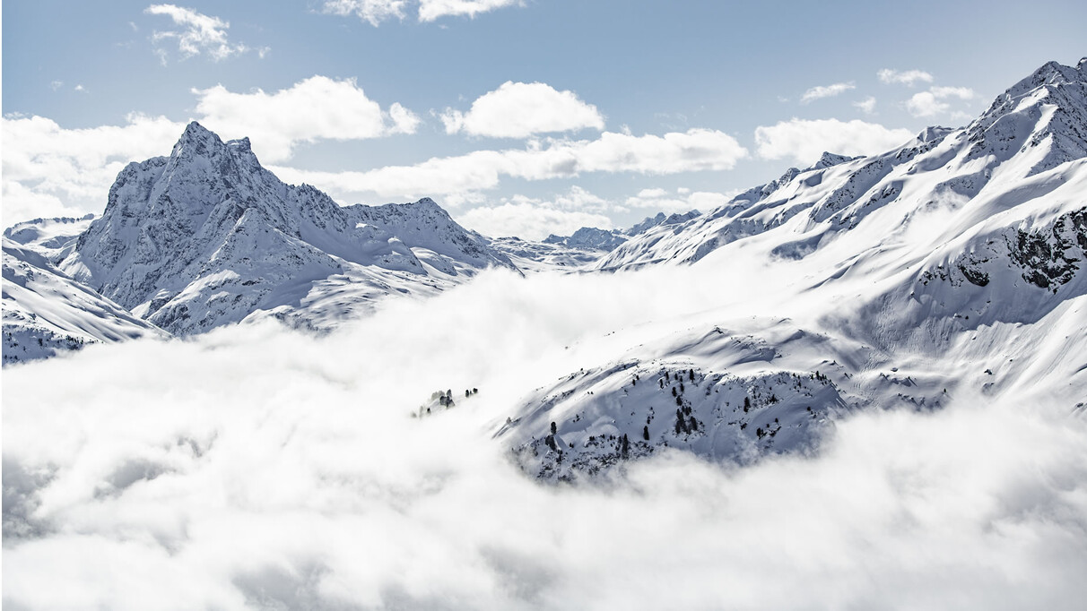 Winter panorama with the striking Patteriol peak and wide, snow-covered slopes under a blue sky.