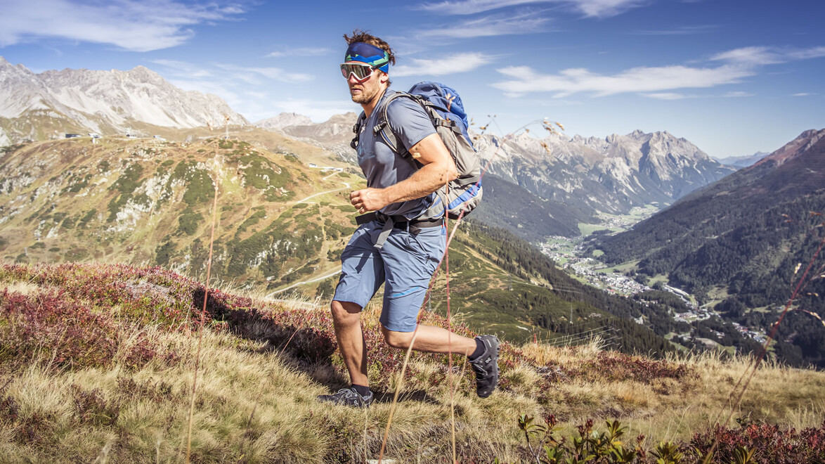 Ein Mann joggt auf einem herbstlichen Berghang mit weitem Blick ins Tal / A man jogs on an autumnal mountain slope with a wide view into the valley