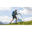 Ein Mann mit Rucksack und Wanderstöcken steigt über eine Wiese bergauf, im Hintergrund ein felsiger Gipfel / A man with a backpack and trekking poles hikes uphill across a meadow with a rocky peak in the background