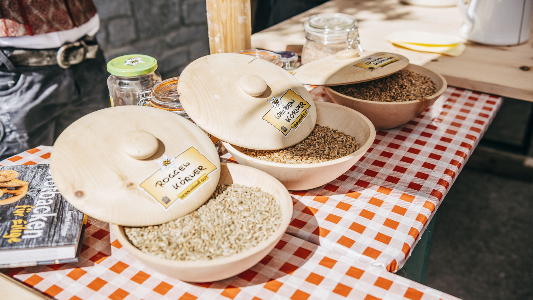 Verschiedene Getreidesorten in Holzgefäßen beschriftet auf kariertem Tuch / Different grains labeled in wooden containers on checkered cloth