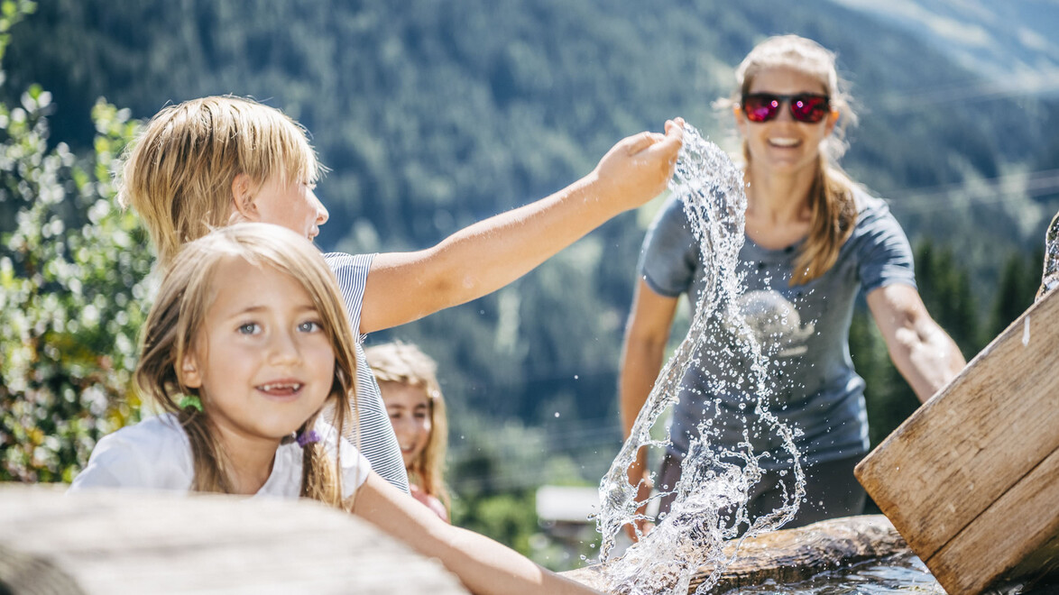 Kinder experimentieren mit Wasser in einer Holzrinne, lachend und neugierig / Children play with water in a wooden channel, smiling and curious