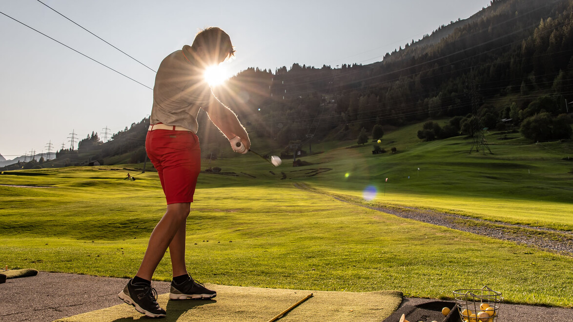 Ein Golfspieler schlägt auf der Driving Range bei Sonnenuntergang ab. / A golfer takes a swing at the driving range during sunset.