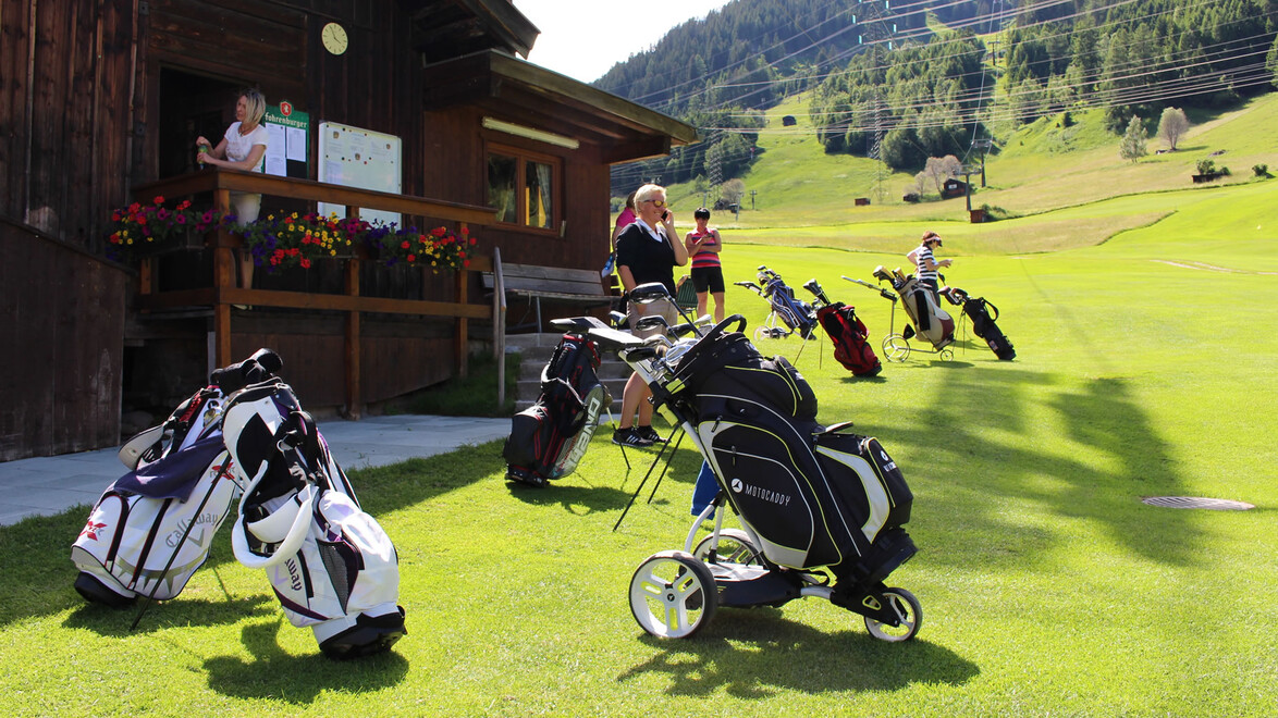 Golfbags stehen vor einem kleinen Clubhaus am Rande des Golfplatzes. / Golf bags are placed in front of a small clubhouse at the edge of the course.
