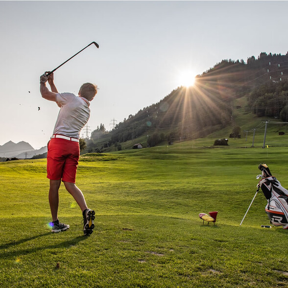 Ein Golfspieler beendet seinen Abschlag auf einem grünen Golfplatz in den Bergen bei Sonnenaufgang.