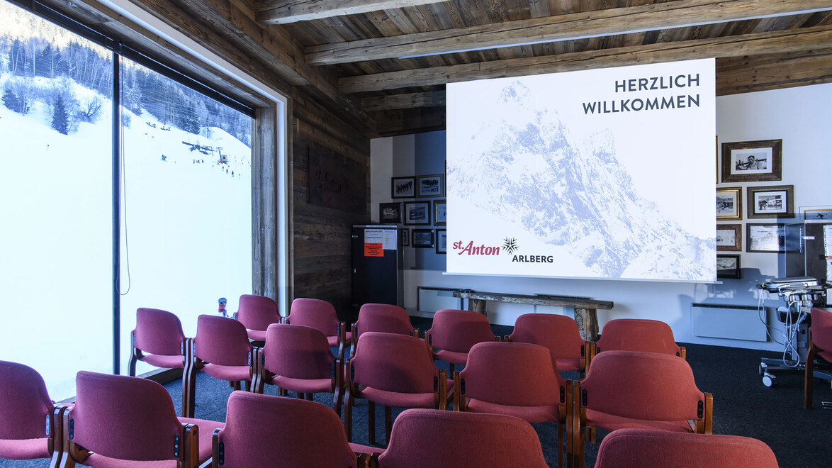 Konferenzraum mit roten Stühlen, Leinwand und Panoramablick auf verschneite Landschaft / Conference room with red chairs, screen and panoramic view of snowy landscape