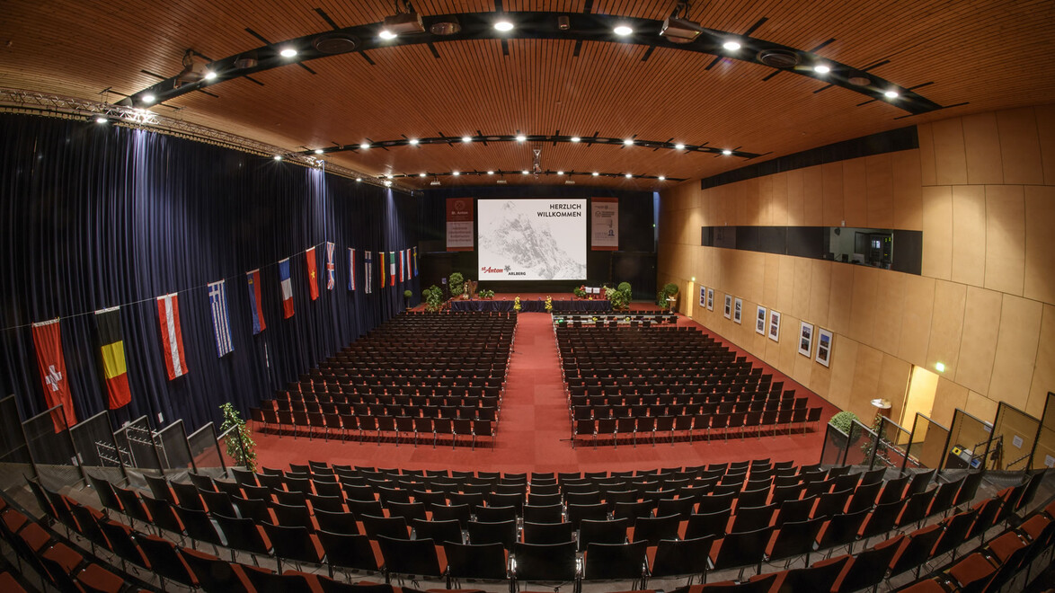 Großer Veranstaltungssaal mit Bühne, Leinwand und vielen Stuhlreihen / Large event hall with stage, screen and many rows of chairs