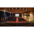 Großer Veranstaltungssaal mit Bühne, Leinwand und vielen Stuhlreihen / Large event hall with stage, screen and many rows of chairs