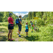 Eine Familie mit Wanderrucksack steht an einem Wegweiser und blickt auf eine Karte im Grünen / A family with hiking backpacks looks at a trail sign and map in a green landscape