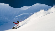 Snowboarder makes turns in fresh powder on an untouched slope.