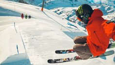 Freeskier jumps off a kicker ramp in the snowpark wearing colorful gear.