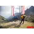 Drei Wanderer stehen bei zwei rot-weiß-roten Fahnen auf einem Bergkamm mit Blick auf die umliegenden Lechtaler Alpen / Three hikers stand next to two red-white-red flags on a mountain ridge overlooking the Lechtal Alps
