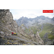 Drei Personen queren einen felsigen Steig mit schroffen Gipfeln im Hintergrund / Three people cross a rocky path with rugged peaks in the background