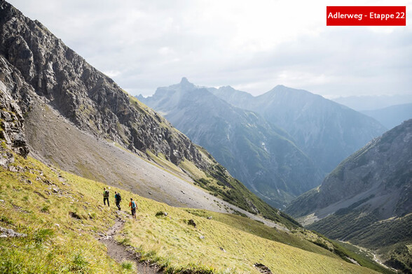 Wanderer auf einem Berghang mit weitem Blick über grüne Täler und ferne Gipfel / Hikers on a mountain slope with a wide view of green valleys and distant peaks