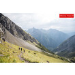 Wanderer auf einem Berghang mit weitem Blick über grüne Täler und ferne Gipfel / Hikers on a mountain slope with a wide view of green valleys and distant peaks