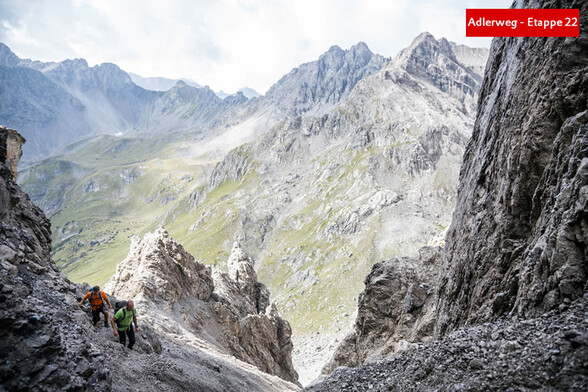 Zwei Personen steigen über ein steiniges Kar inmitten steiler Felswände auf / Two people ascend through a rocky cirque surrounded by steep cliffs
