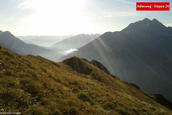 Morgensonne scheint über einen grasbewachsenen Kamm mit Blick ins Tal / Morning sun shines over a grassy ridge with a valley view