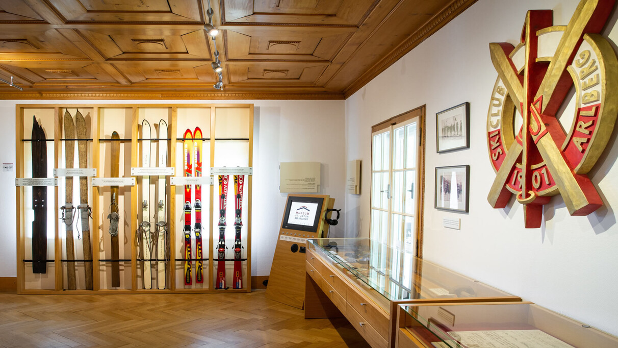 Innenansicht des Skimuseums St. Anton am Arlberg mit historischen Skiern, Holzelementen, Infotafeln und einem Touchscreen.