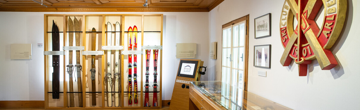  Innenansicht des Skimuseums St. Anton am Arlberg mit historischen Skiern, Holzelementen, Infotafeln und einem Touchscreen.