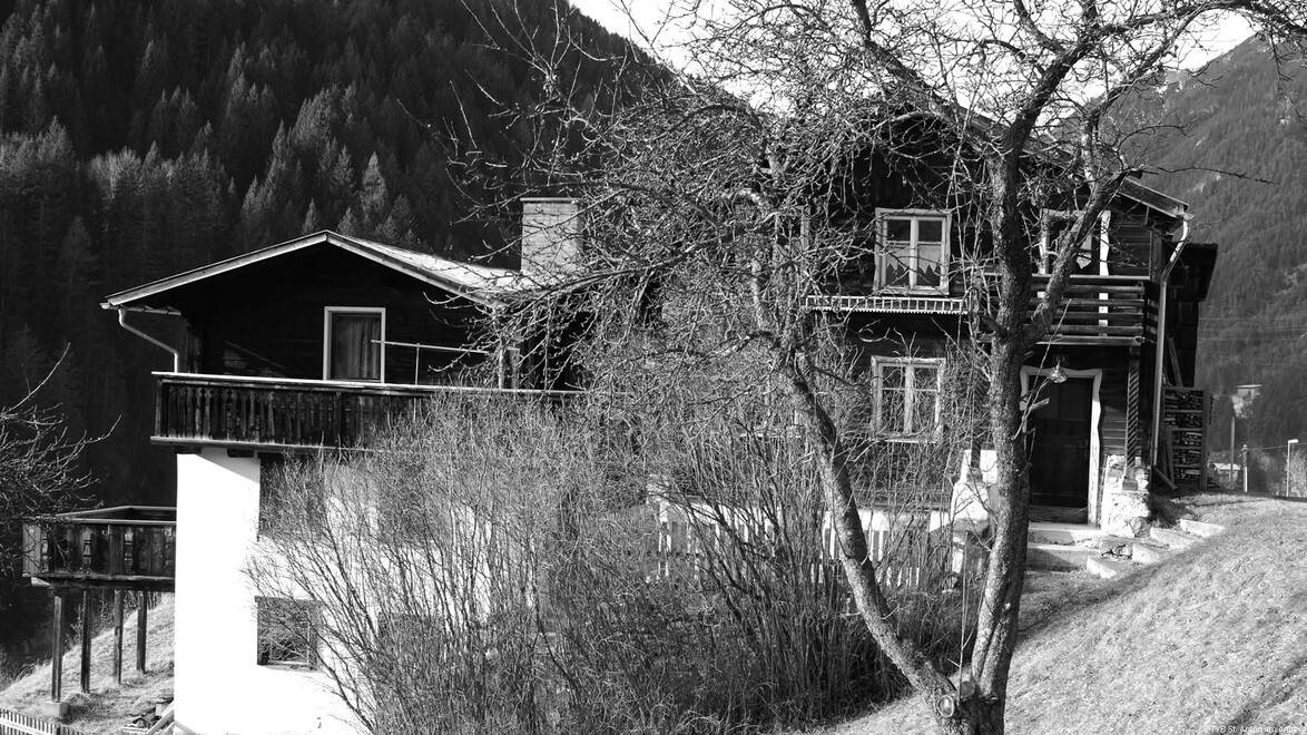 Altes Holzhaus mit Balkon und Baum im Vordergrund, Hanglage / Old wooden house with balcony and tree in front, hillside location
