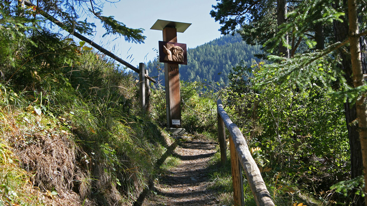 Eine rostfarbene Figur mit Buch auf einem schmalen Waldpfad mit Geländer / A rust-colored figure with an open book on a narrow forest path with railing