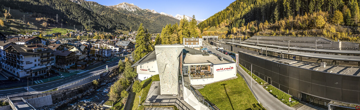 Das arl.park Sport- und Kletterzentrum in St. Anton am Arlberg mit großem Outdoor-Kletterturm, Blick auf den Ort und umliegende Herbstberge.
