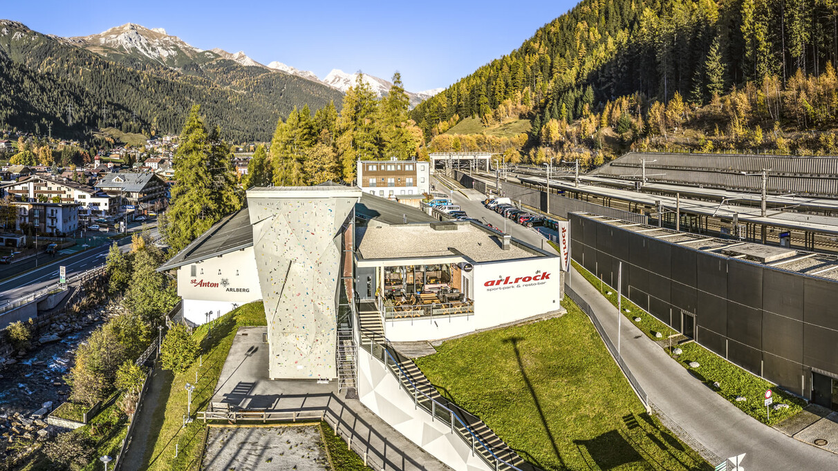 Das arl.park Sport- und Kletterzentrum in St. Anton am Arlberg mit großem Outdoor-Kletterturm, Blick auf den Ort und umliegende Herbstberge.