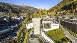 The arl.park sports and climbing center in St. Anton am Arlberg with a large outdoor climbing tower, overlooking the town and autumn mountains.