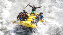 Group of adventurers whitewater rafting on a rushing river near St. Anton am Arlberg, in a yellow inflatable raft led by a guide.