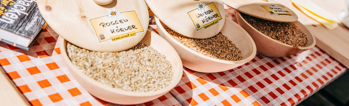 Roggen-, Weizen- und Dinkelkörner in Holzschalen auf einem Markttisch beim Kräuterfest in St. Anton.