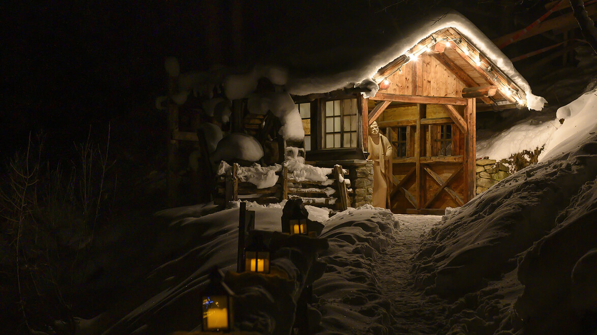 Verschneite Holzhütte mit warmem Licht und leuchtenden Laternen im Vordergrund / Snow-covered wooden cabin with warm light and glowing lanterns in front