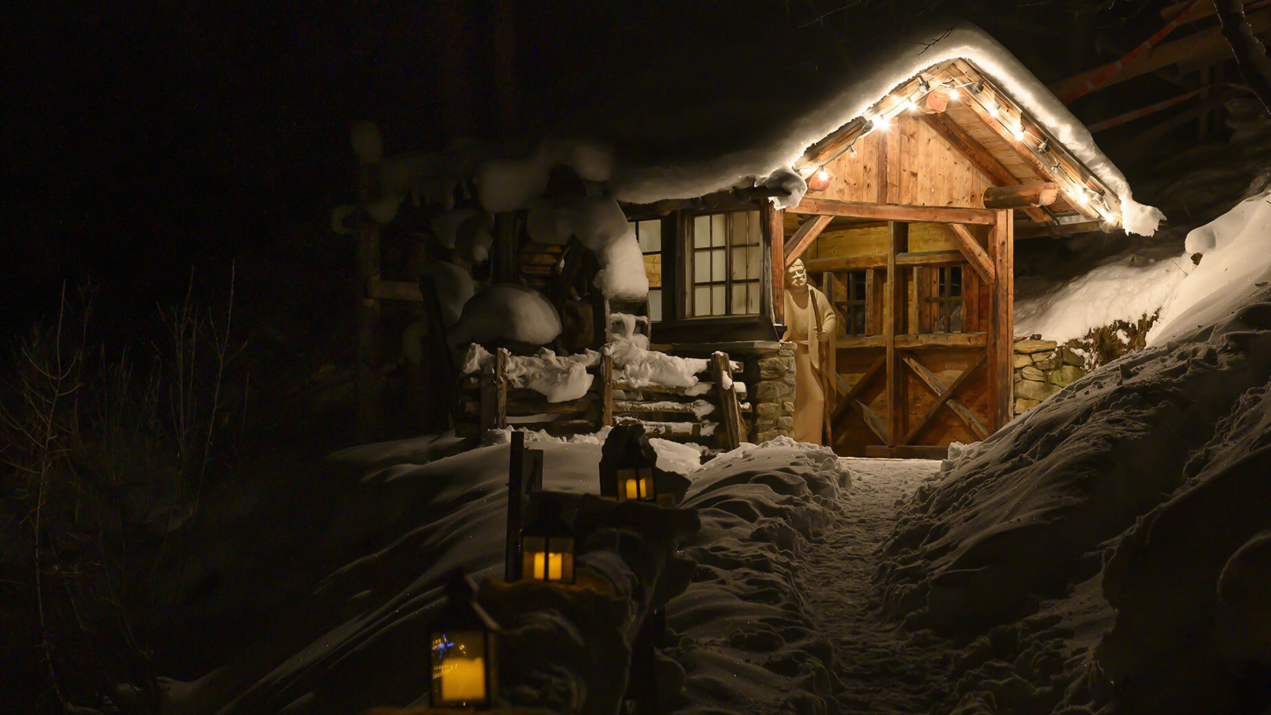 Adventhütte bei Nacht / Christmas cabin at night Verschneite Holzhütte mit warmem Licht und leuchtenden Laternen im Vordergrund / Snow-covered wooden cabin with warm light and glowing lanterns in front