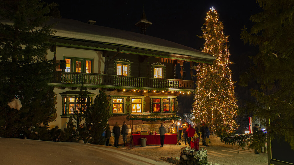 Beleuchtetes Haus mit geschmücktem Weihnachtsbaum und Menschen davor / Lit-up house with decorated Christmas tree and people in front
