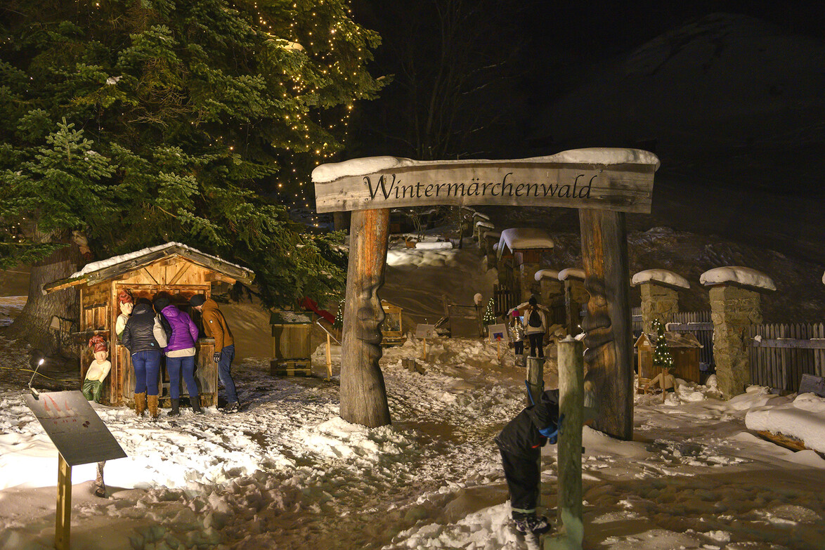 Adventweg mit Krippe, Holzportal und Besuchern im Schnee bei Nacht / Advent path with nativity scene, wooden gate and visitors in the snow at night