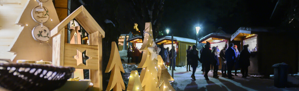 Christmas market with lit wooden stalls and decorations at night in a snowy setting.