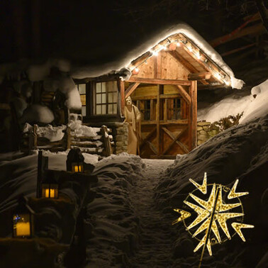 Eine stimmungsvoll beleuchtete Holzhütte im Schnee lädt beim Adventzauber in St. Anton am Arlberg zum Verweilen ein. Der Pfad ist mit Kerzen gesäumt und schafft eine festliche Atmosphäre.
