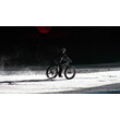 Eine Person fährt mit einem Fatbike auf der verschneiten Piste bei Dunkelheit. / A person rides a fatbike on a snowy slope in the dark.