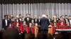Ein Knabenchor und Männerchor singen gemeinsam unter der Leitung eines Dirigenten auf einer Bühne / A boys’ and men’s choir perform together under a conductor on stage
