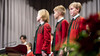 Drei Knaben in roten Uniformen stehen nebeneinander auf der Bühne beim Singen / Three boys in red uniforms stand side by side on stage while singing
